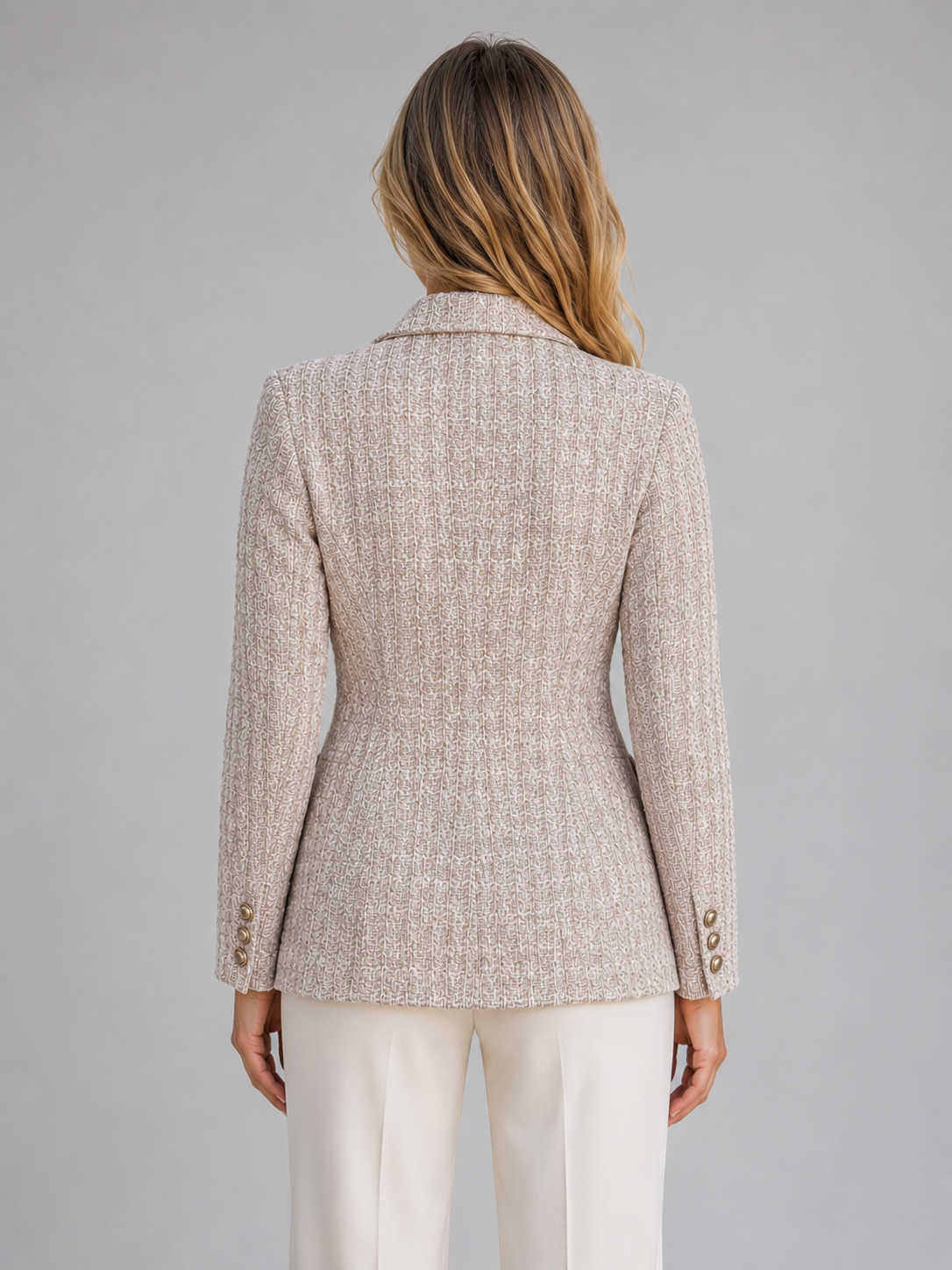 Woman wearing beige tweed double breasted blazer with white trousers, back view showing tailored fit and button details