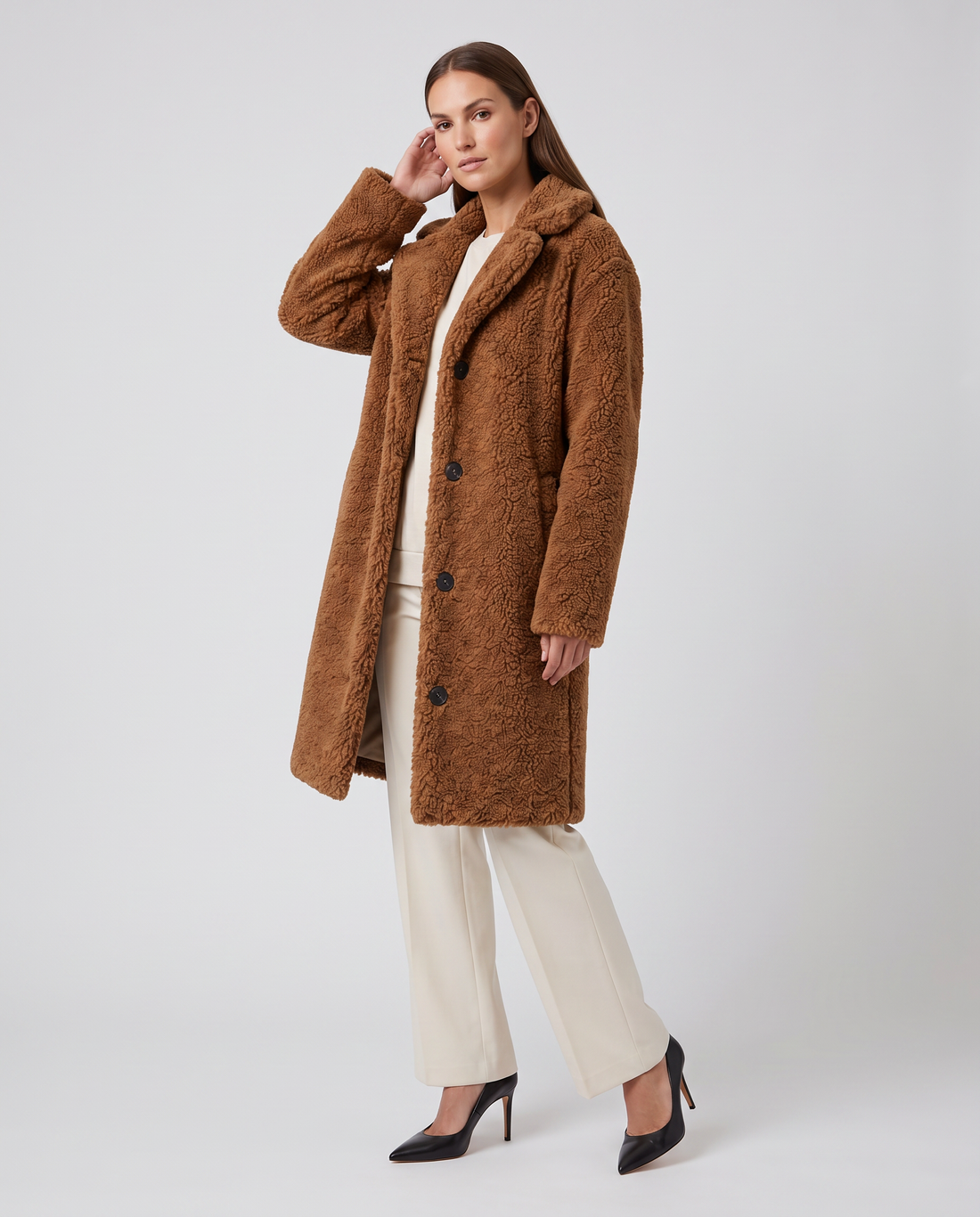 Woman wearing camel brown single-breasted teddy coat with cream pants and black pointed-toe heels