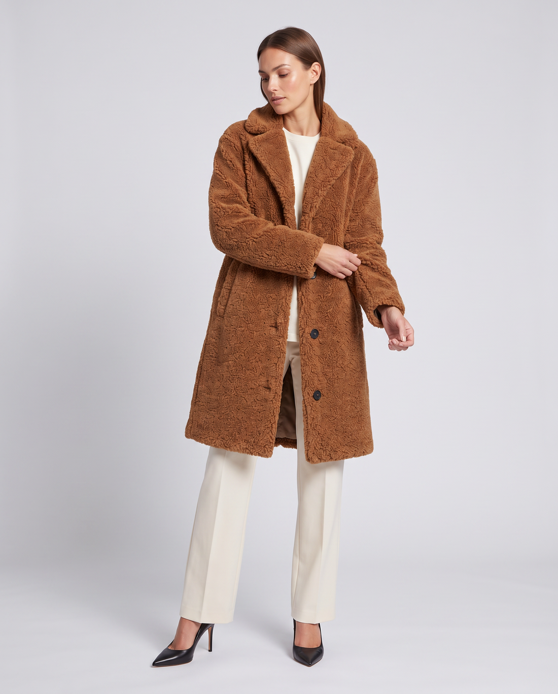 Woman wearing camel teddy coat over cream pants and black heels, single breasted with notch collar and button front