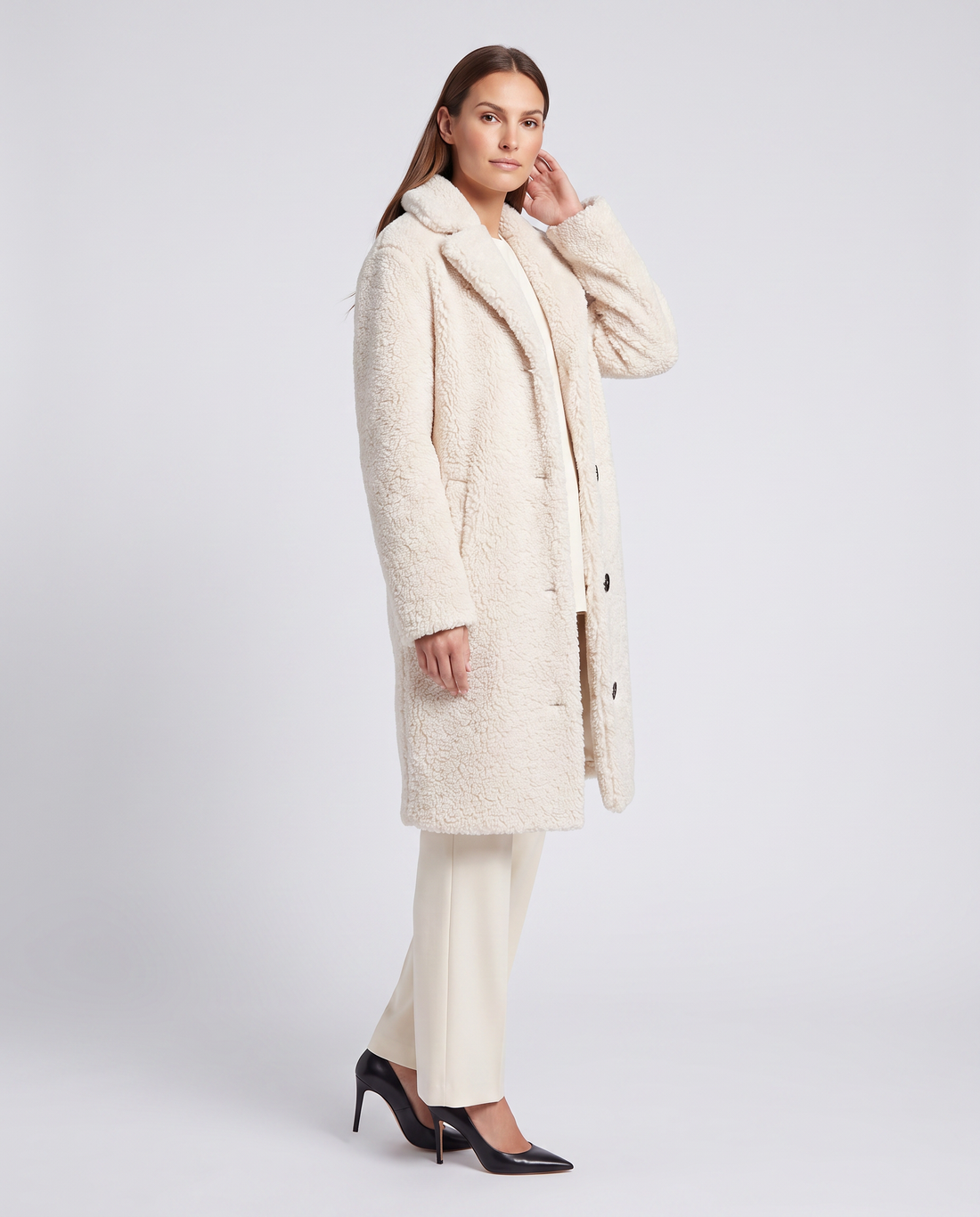 Woman wearing cream teddy coat with collar, buttons, and long sleeves, paired with white pants and black high heels