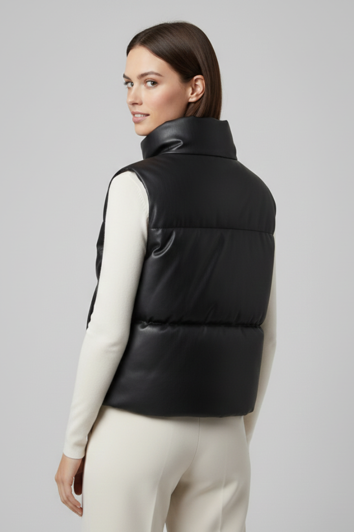 Woman wearing black sleeveless puffer vest with high neckline over cream long-sleeve top and beige pants, shown from back angle