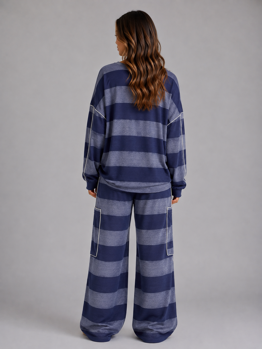 Woman wearing navy and gray striped oversized sweatshirt and matching wide leg lounge trousers with white piping detail, shown from behind