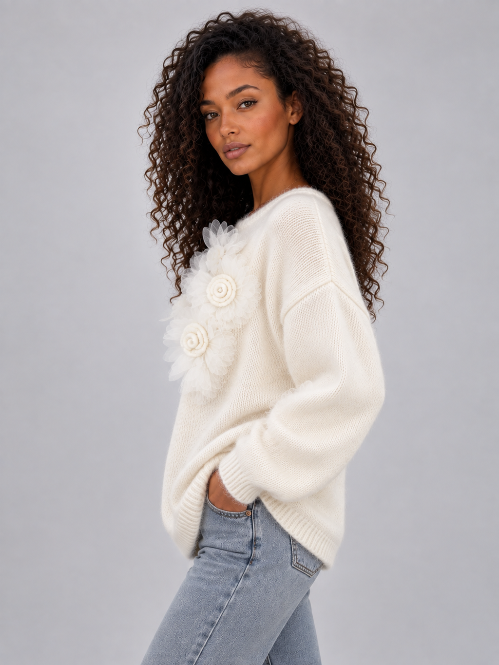 Woman wearing cream crew neck knit jumper with white 3D floral details, paired with light blue jeans