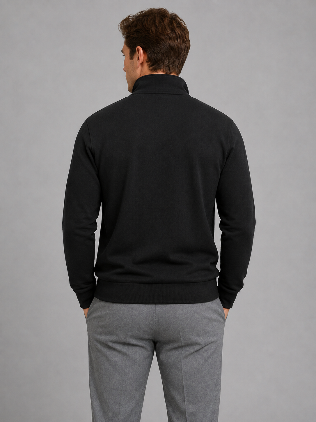 Man wearing black half-zip pullover sweatshirt with high neck and gray trousers, shown from back view against gray background