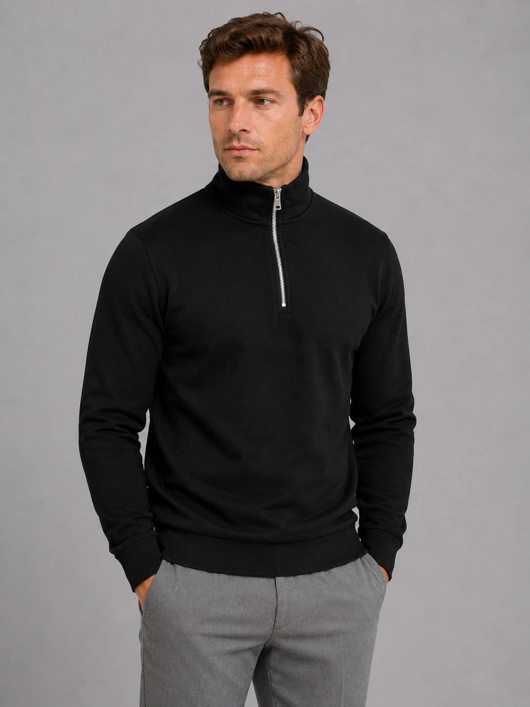 Man wearing black high neck half-zip pullover sweatshirt with gray pants against gray background