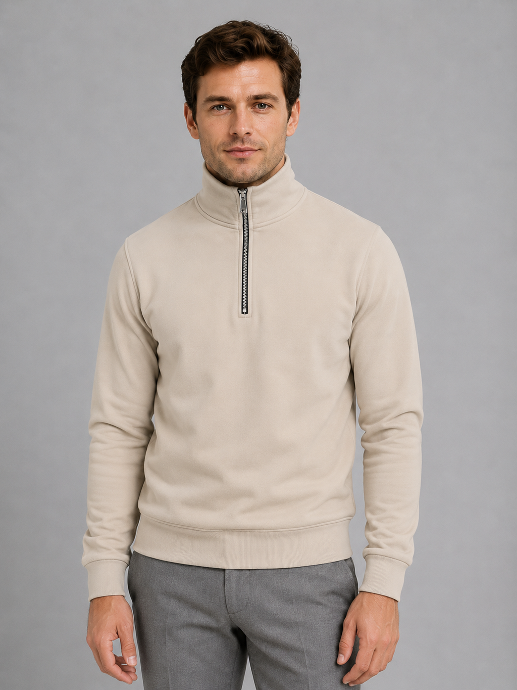 Man wearing cream high neck half-zip pullover sweatshirt with gray pants against gray background