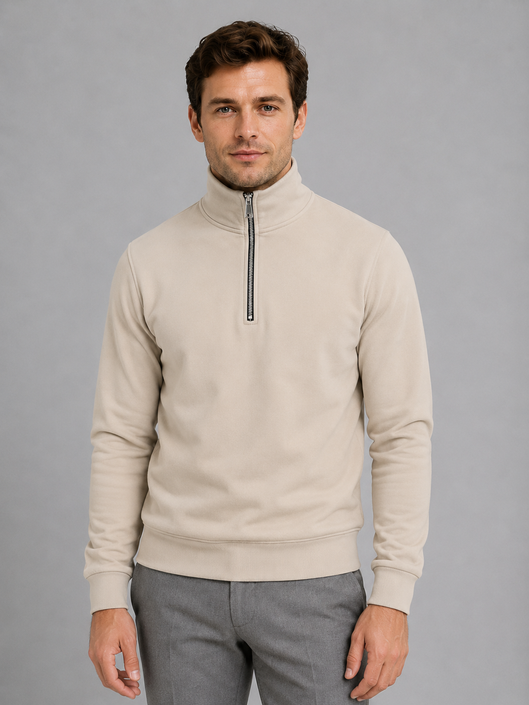 Man wearing cream high neck half-zip pullover sweatshirt with gray pants against gray background