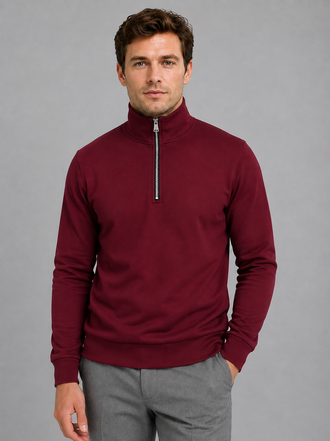 Man wearing maroon high neck half-zip pullover sweatshirt with gray pants against gray background