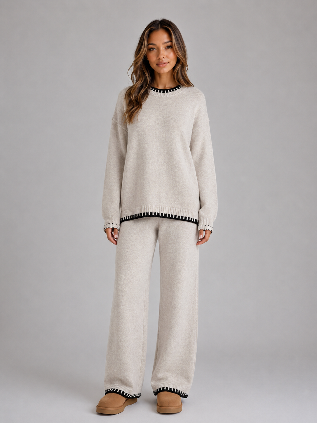 Woman wearing cream knitted jumper and wide leg trousers co-ord set with black and white stripe trim detail and tan platform boots