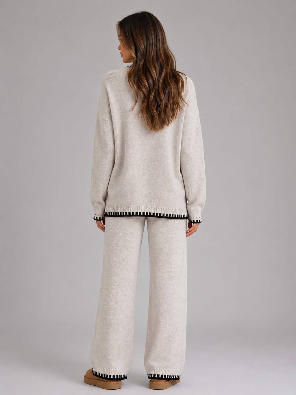 Woman wearing cream relaxed wide leg trousers and matching knitted jumper with black striped trim cuffs, back view