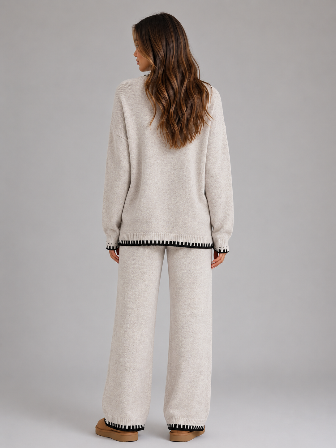 Woman wearing cream relaxed wide leg trousers and matching knitted jumper with black striped trim cuffs, back view