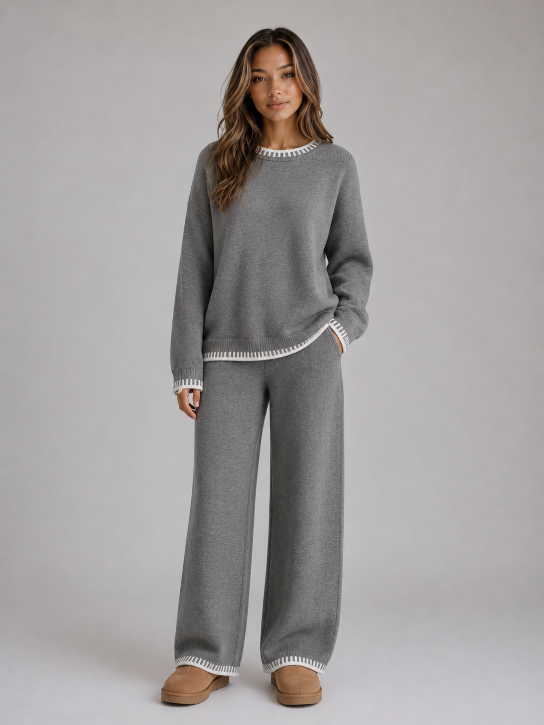Woman wearing gray knitted jumper with white trim and matching wide leg trousers, styled with tan platform slippers