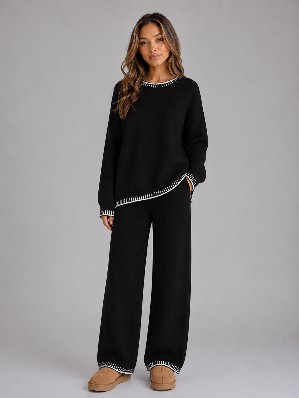 Woman wearing black knit sweater and wide leg trousers with white stripe trim, paired with tan platform slippers