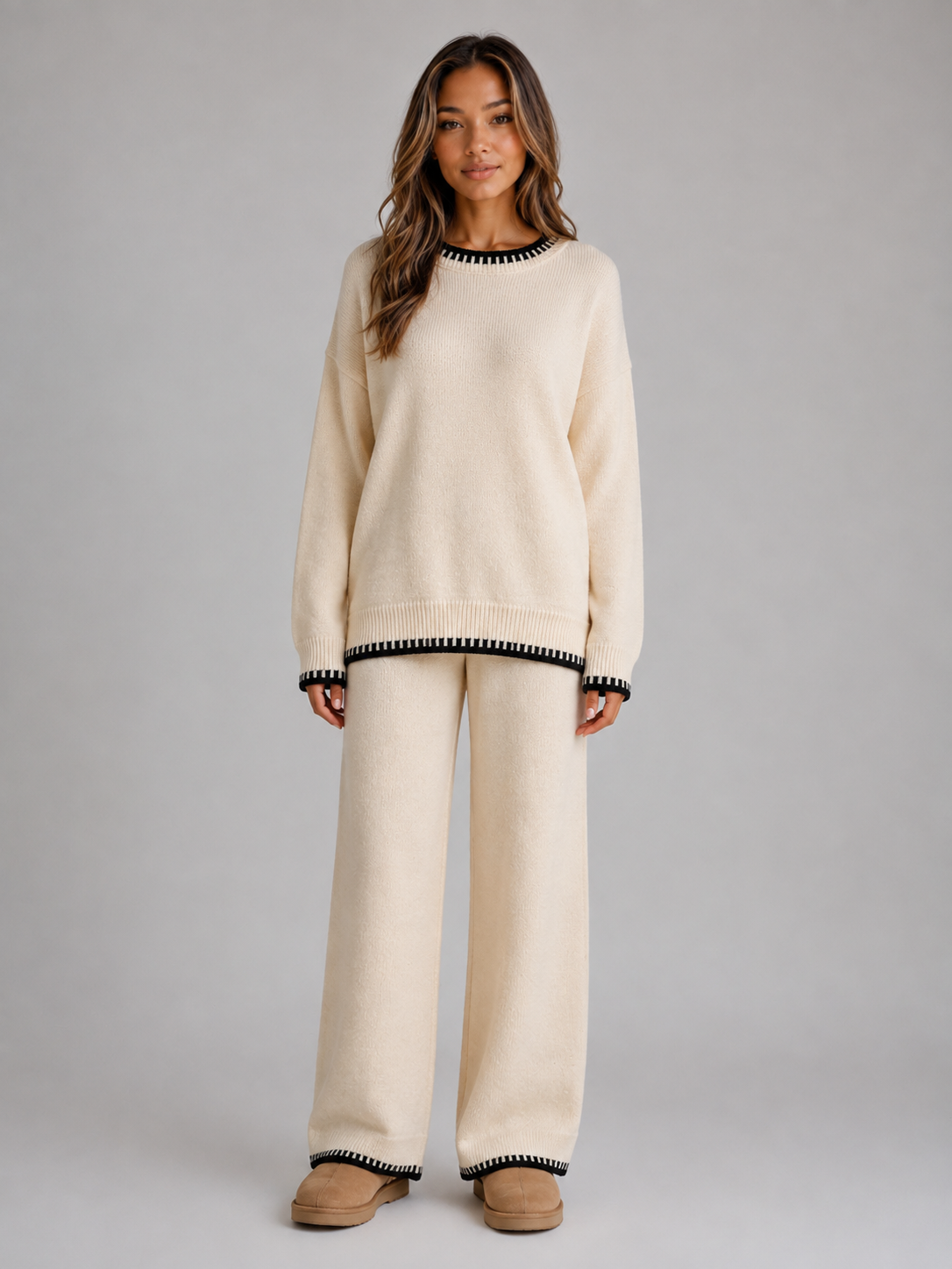 Woman wearing cream knitted jumper and wide leg trousers set with black trim details, styled with tan slippers