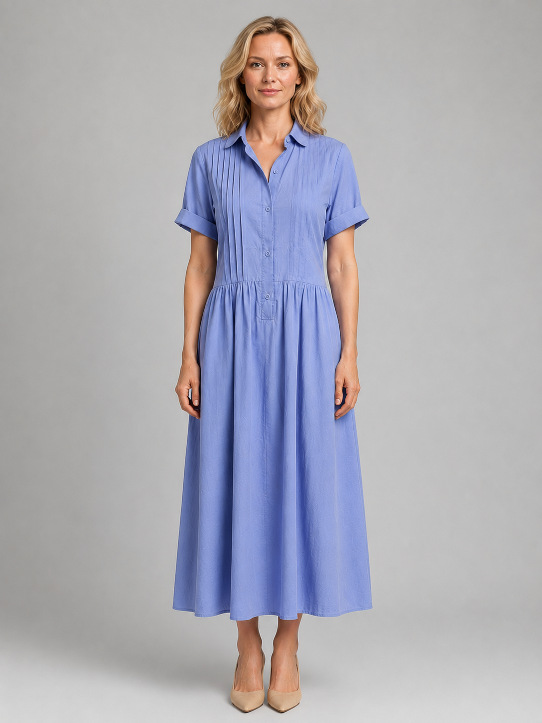 Woman wearing a light blue pleated button-up maxi dress with short sleeves and pockets, styled with nude heels