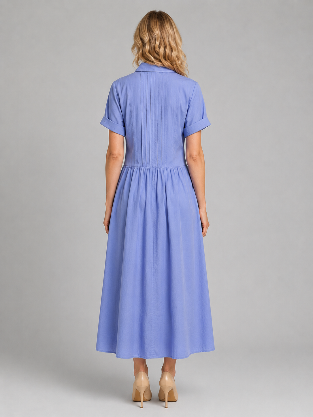 Woman wearing light blue pleated short-sleeve maxi shirt dress with pockets, shown from back, styled with tan heels