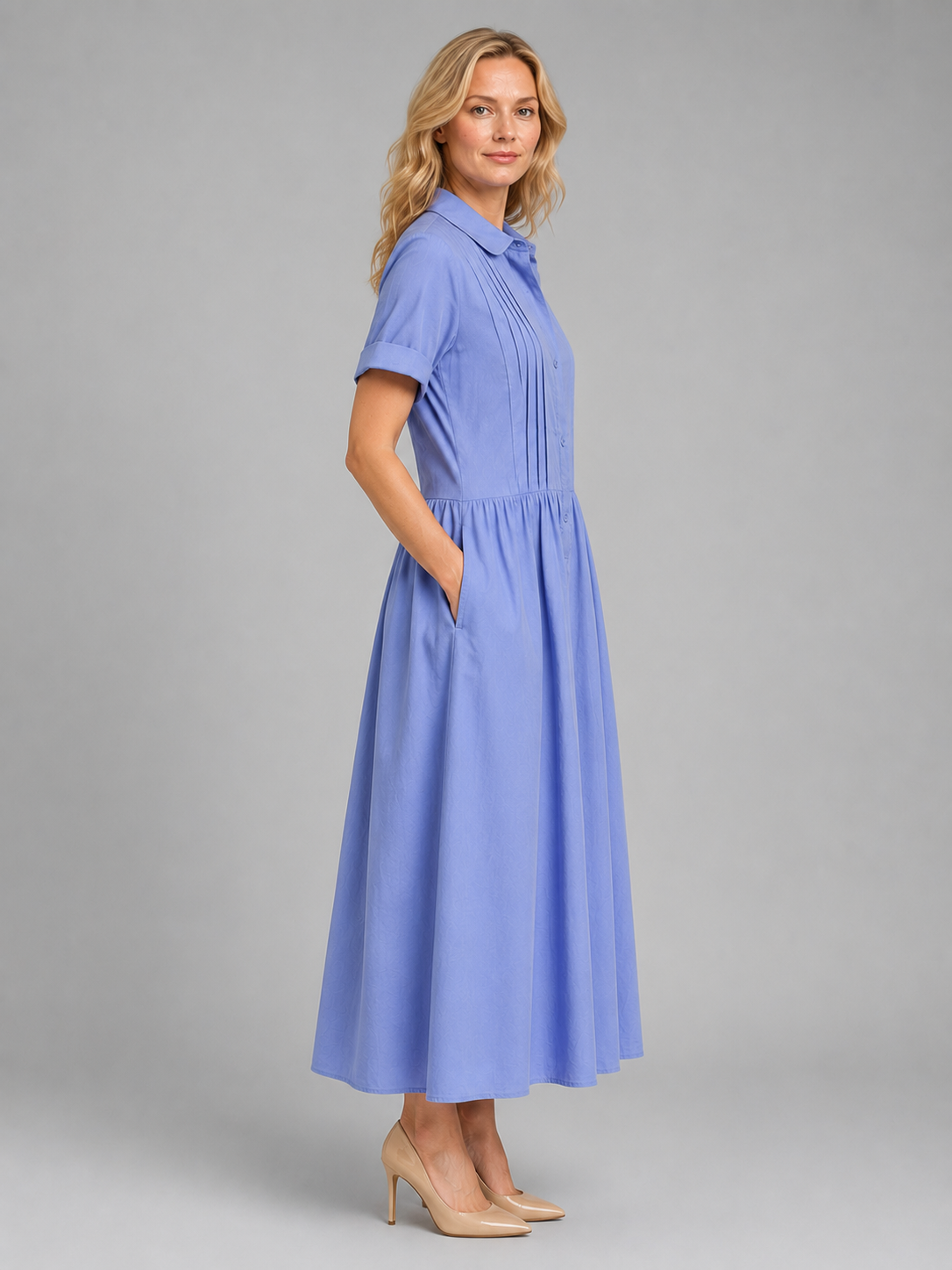Woman wearing periwinkle blue relaxed pleated shirt maxi dress with short sleeves and pockets, styled with beige heels