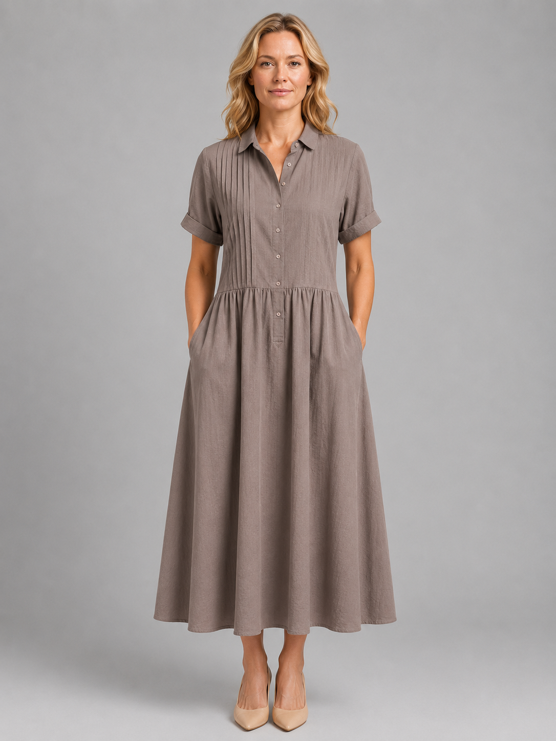 Woman wearing a taupe pleated button-front maxi dress with short sleeves and pockets, styled with nude heels