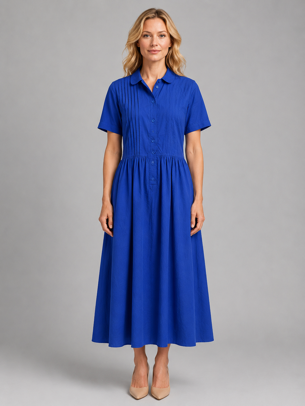 Woman wearing blue short-sleeved pleated shirt maxi dress with pockets and button front, paired with beige heels
