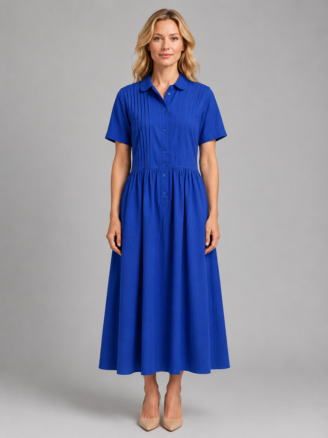 Woman wearing blue short-sleeved pleated shirt maxi dress with pockets and button front, paired with beige heels
