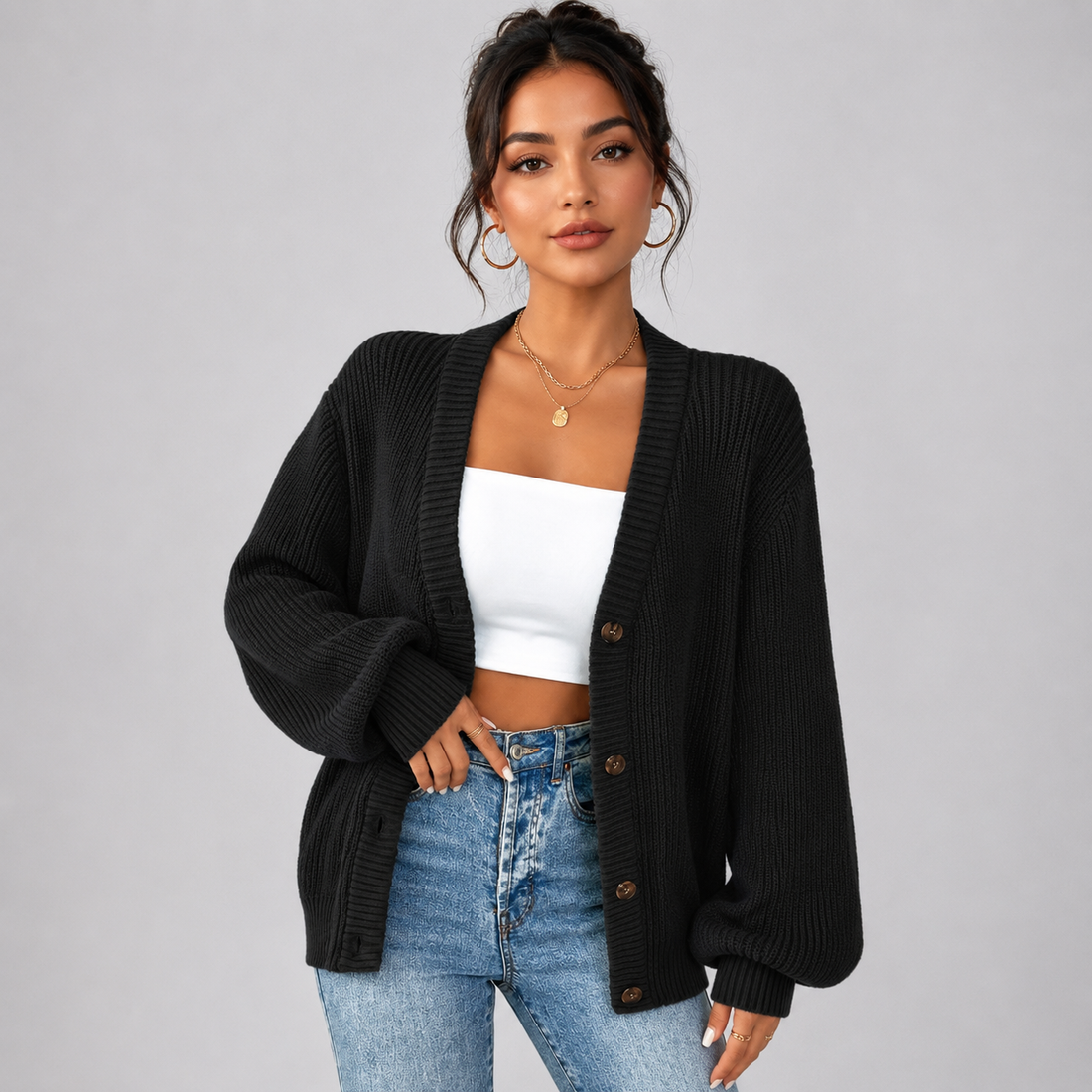 Woman wearing black ribbed v-neck cardigan with brown buttons over white crop top and blue jeans