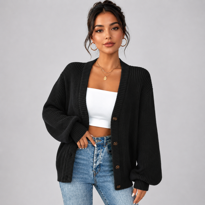 Woman wearing black ribbed v-neck cardigan with brown buttons over white crop top and blue jeans