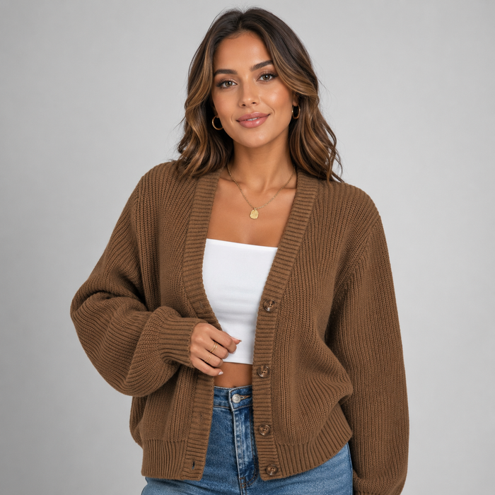 Woman wearing tan ribbed v-neck cardigan with button front over white crop top and blue jeans