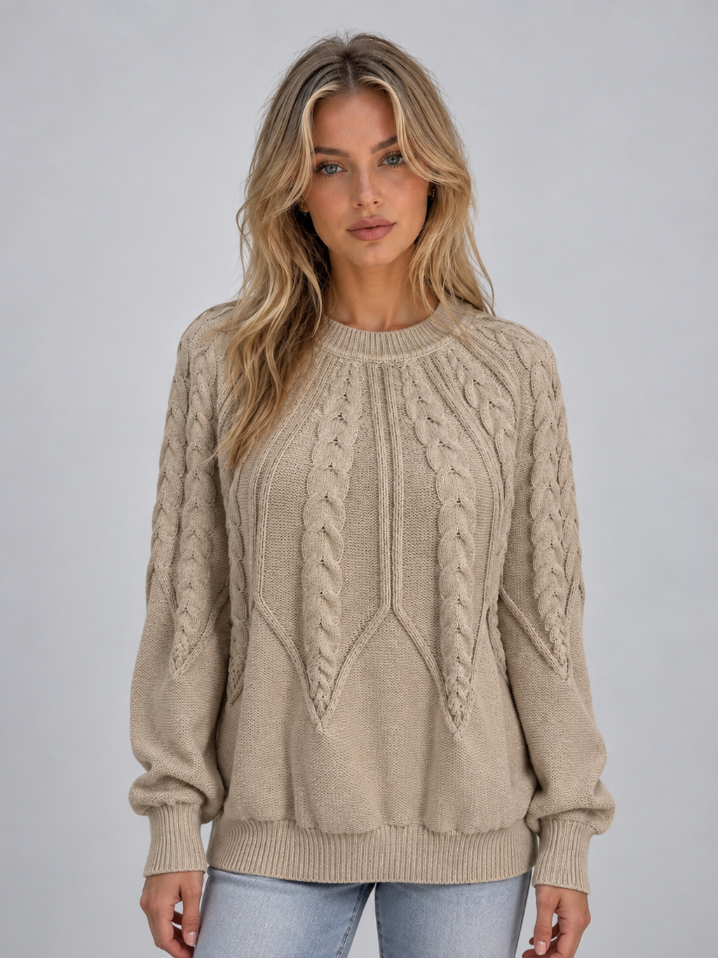 Woman wearing beige cable knit crew neck sweater with long sleeves and ribbed cuffs, styled with light blue jeans