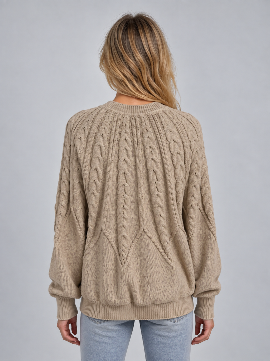 Woman wearing beige cable knit crew neck sweater with long sleeves and ribbed cuffs, shown from back