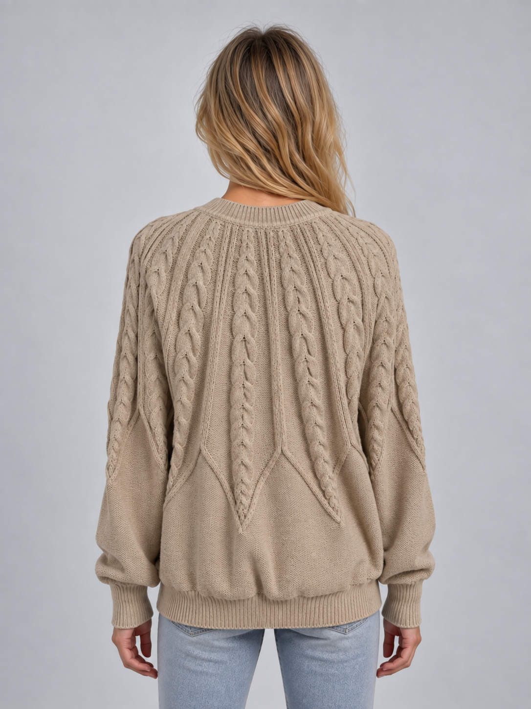 Woman wearing beige cable knit crew neck sweater with long sleeves and ribbed cuffs, shown from back