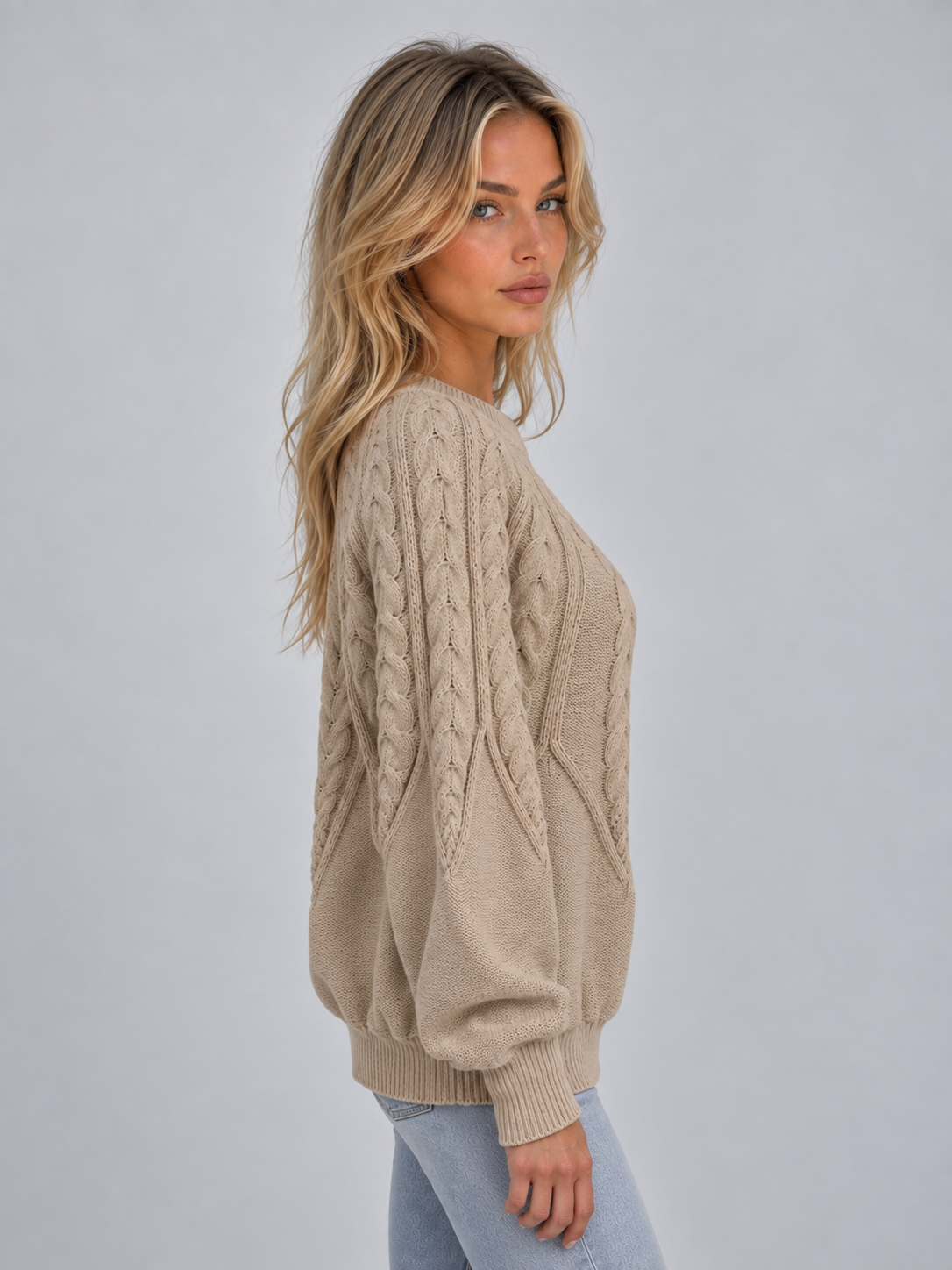 Woman wearing beige cable knit crew neck jumper with long sleeves, paired with light blue jeans, shown from side angle