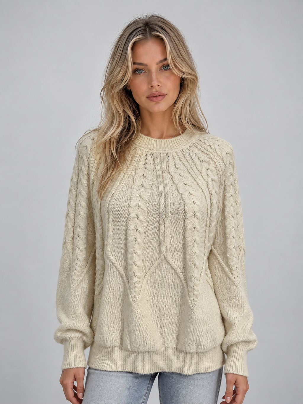 Woman wearing cream cable knit crew neck sweater with long sleeves and ribbed cuffs, paired with light blue jeans