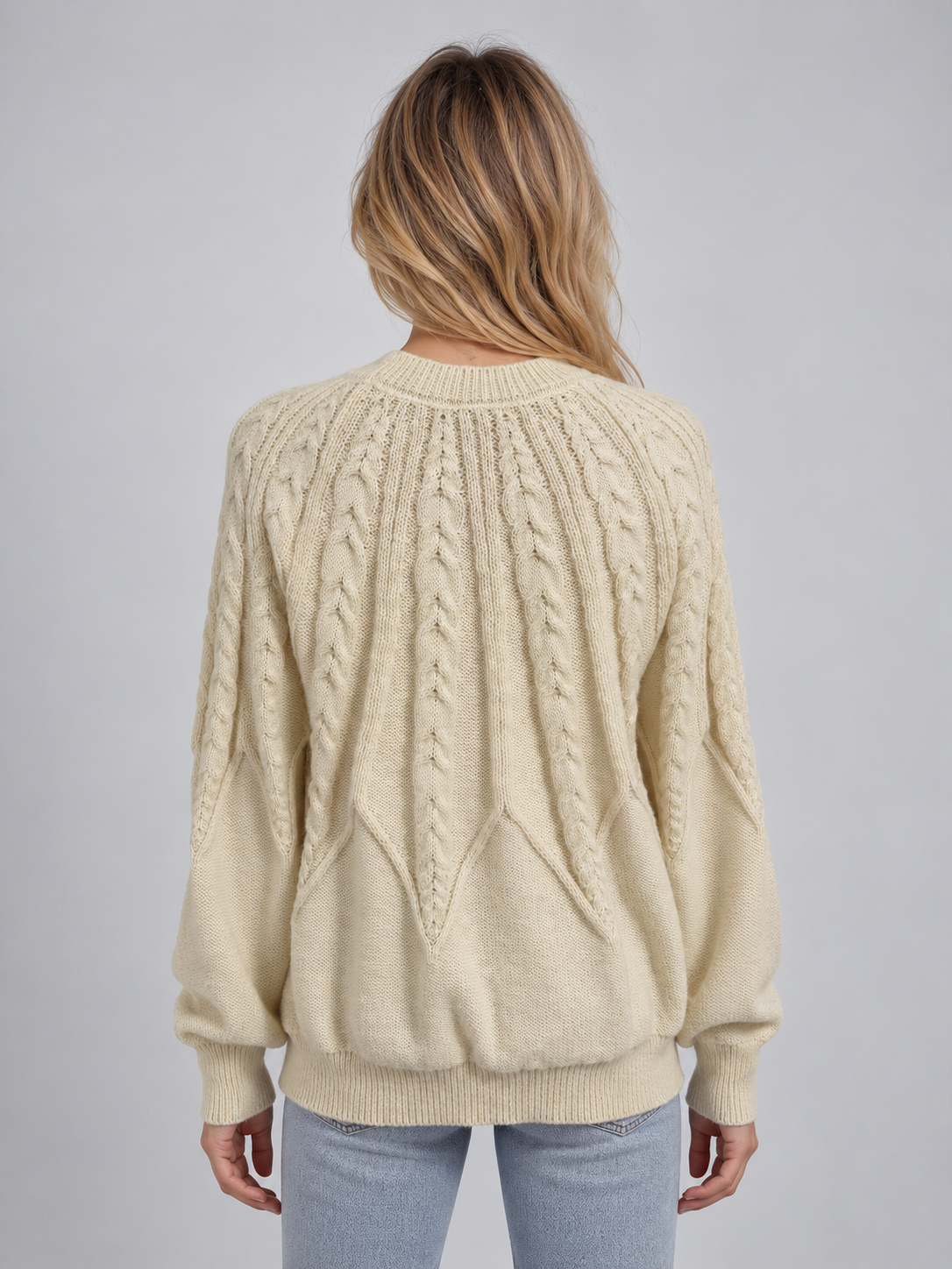 Woman wearing cream cable knit crew neck jumper with long sleeves and ribbed cuffs, shown from back view with light blue jeans