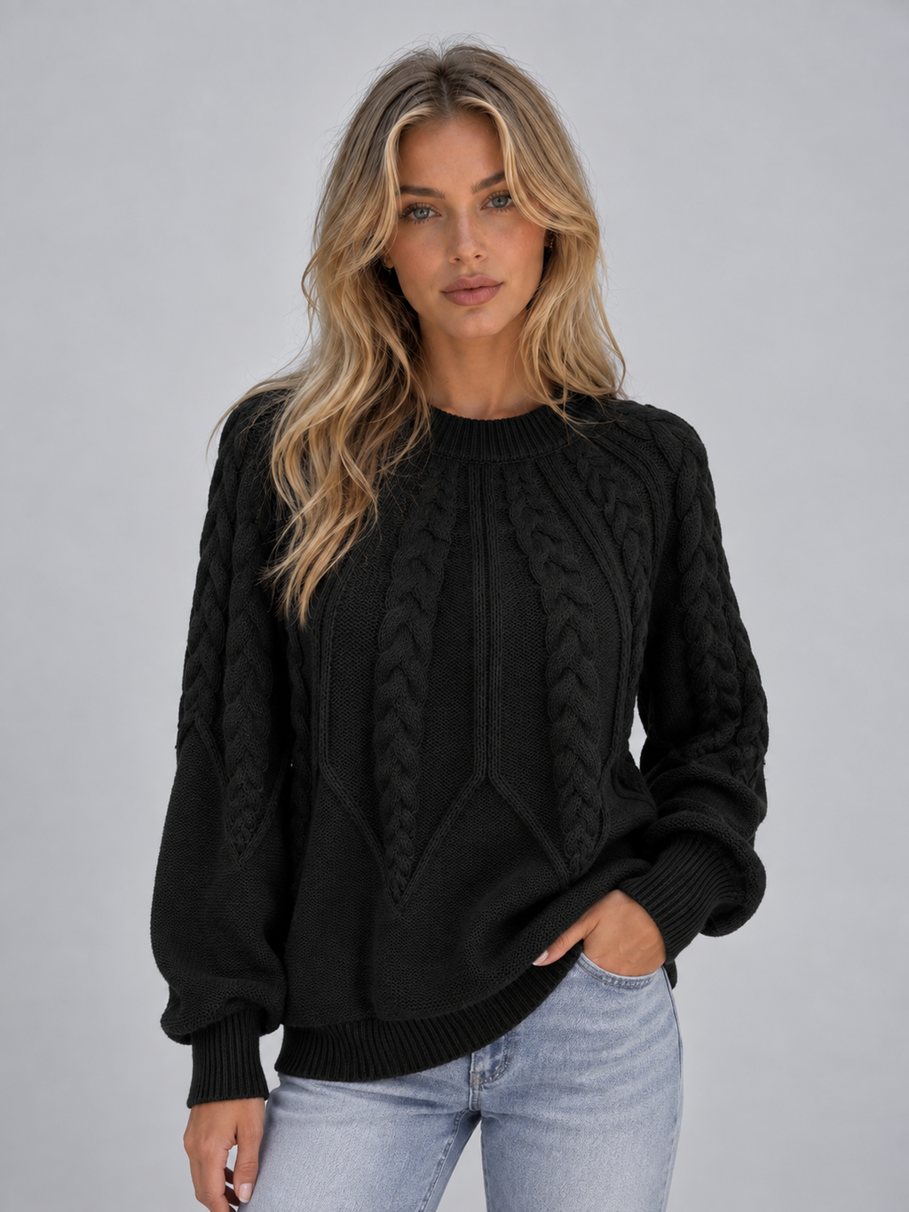 Woman wearing black cable knit crew neck sweater with light blue jeans against gray background