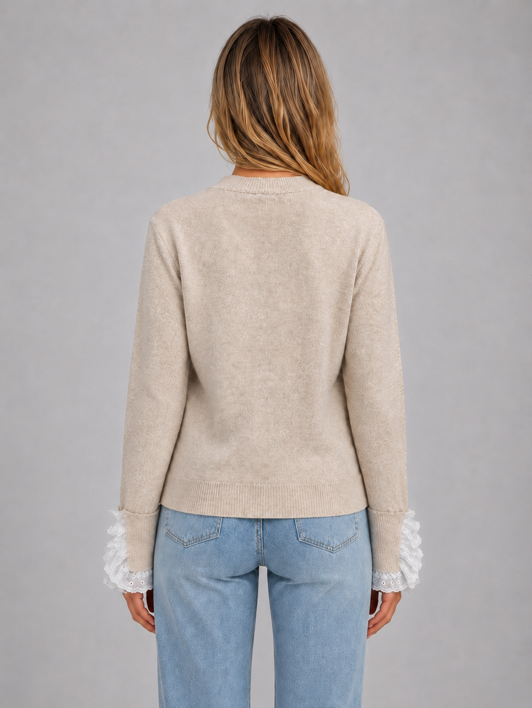 Woman wearing beige crew neck knitted jumper with lace trim sleeves and light blue jeans, back view
