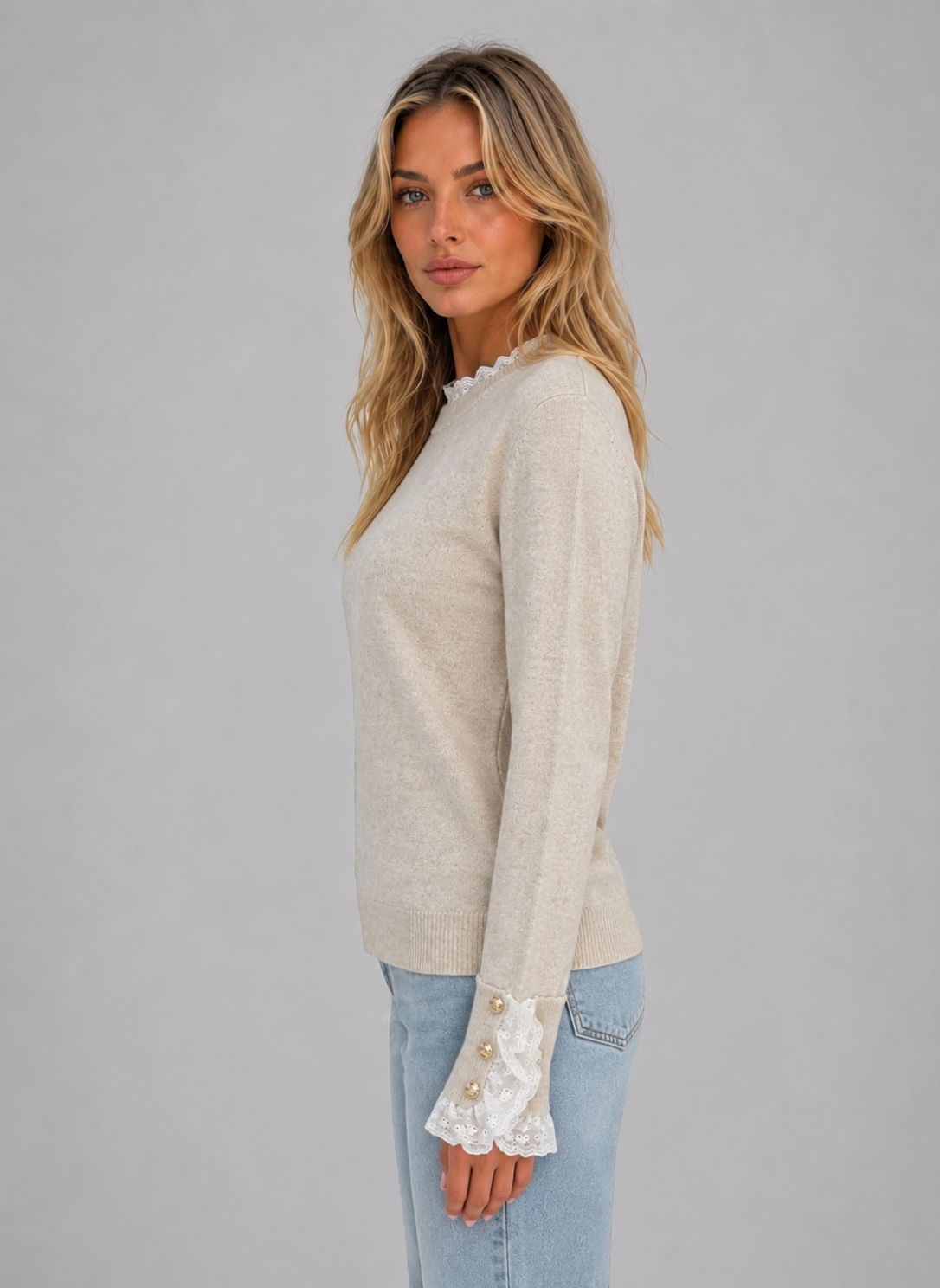 Woman wearing beige crew neck long sleeve knitted jumper with white lace trim cuffs and light blue jeans
