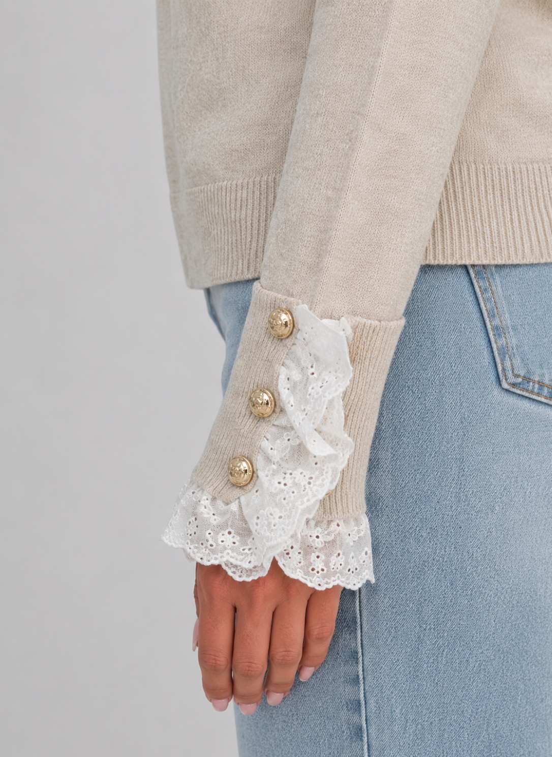 Beige knitted jumper with white lace-trimmed cuffs and gold buttons, worn with light blue jeans