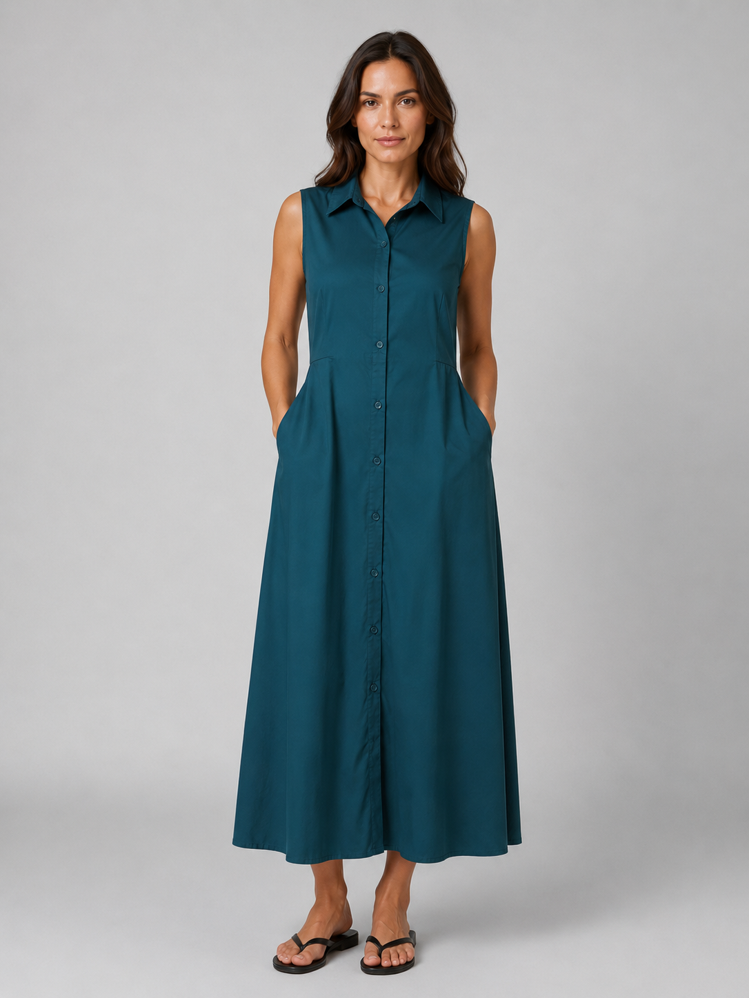 Woman wearing teal sleeveless button-front maxi shirt dress with pockets and collar, paired with black slide sandals