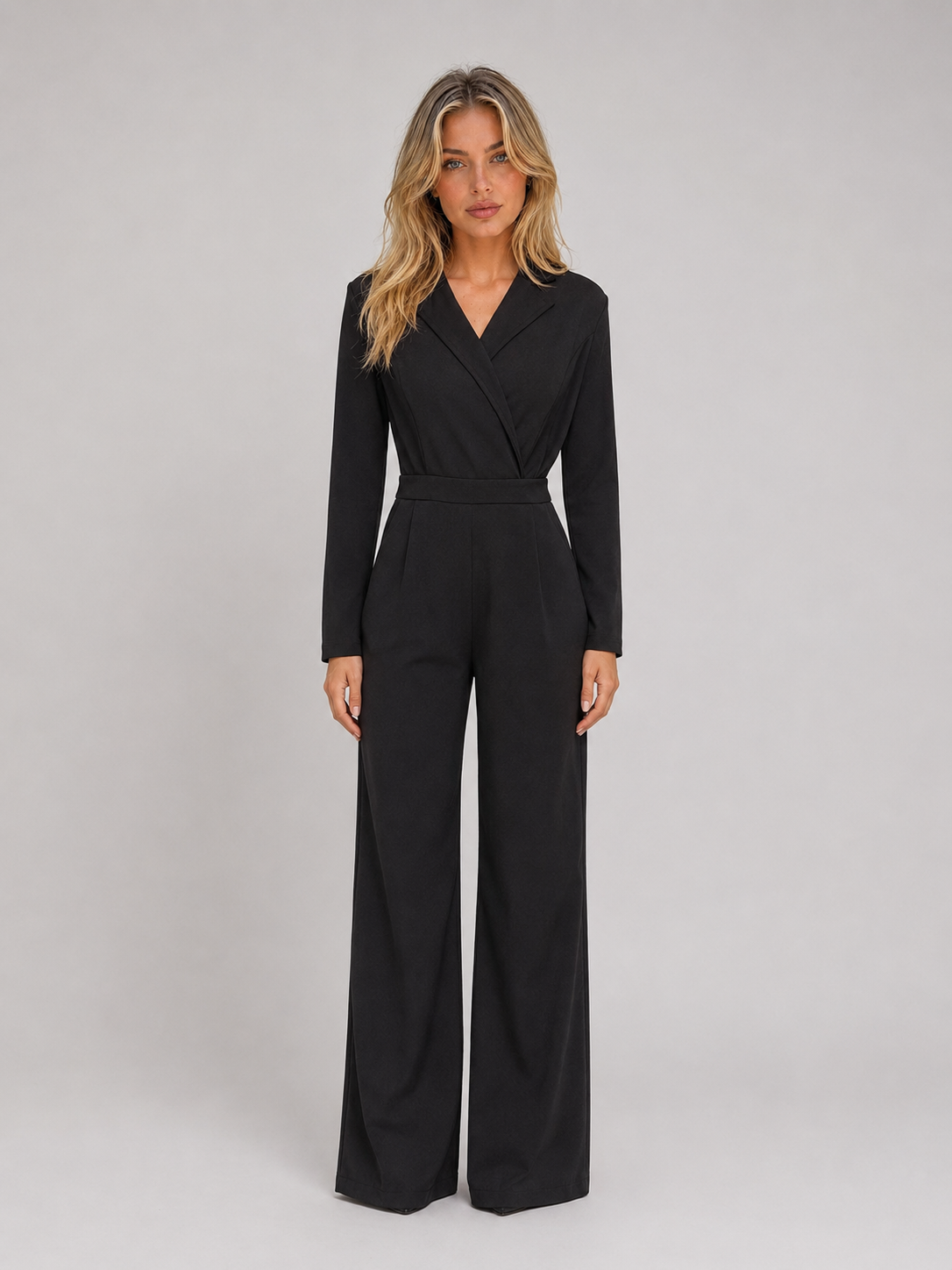 Woman wearing black belted wrap front wide leg jumpsuit with long sleeves against white background