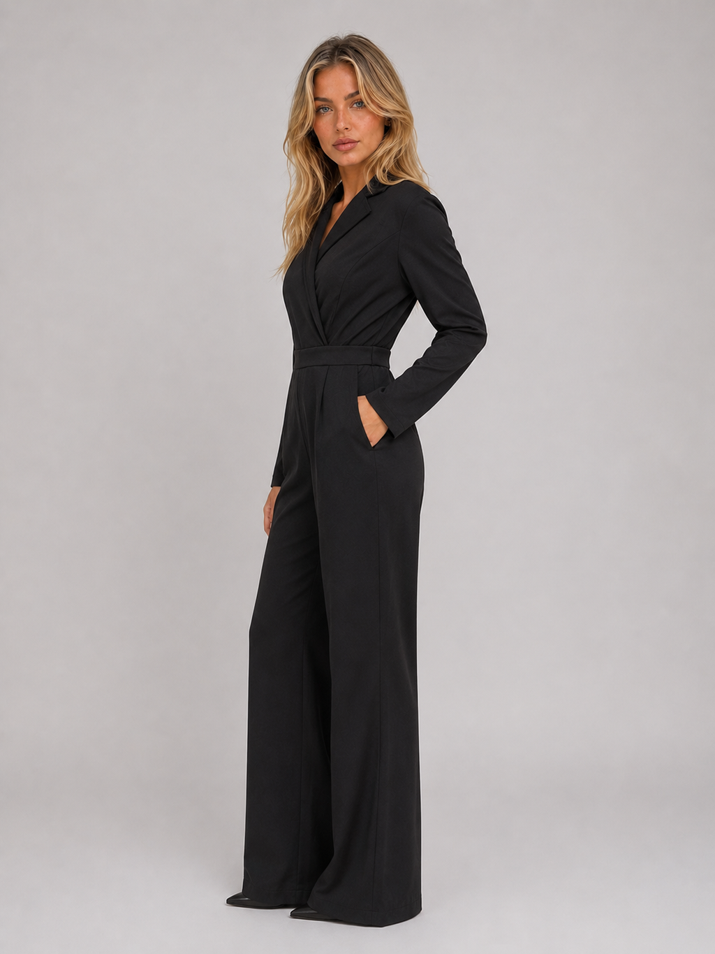 Woman wearing black belted tailored wrap front wide leg jumpsuit with long sleeves and pockets, standing against neutral background