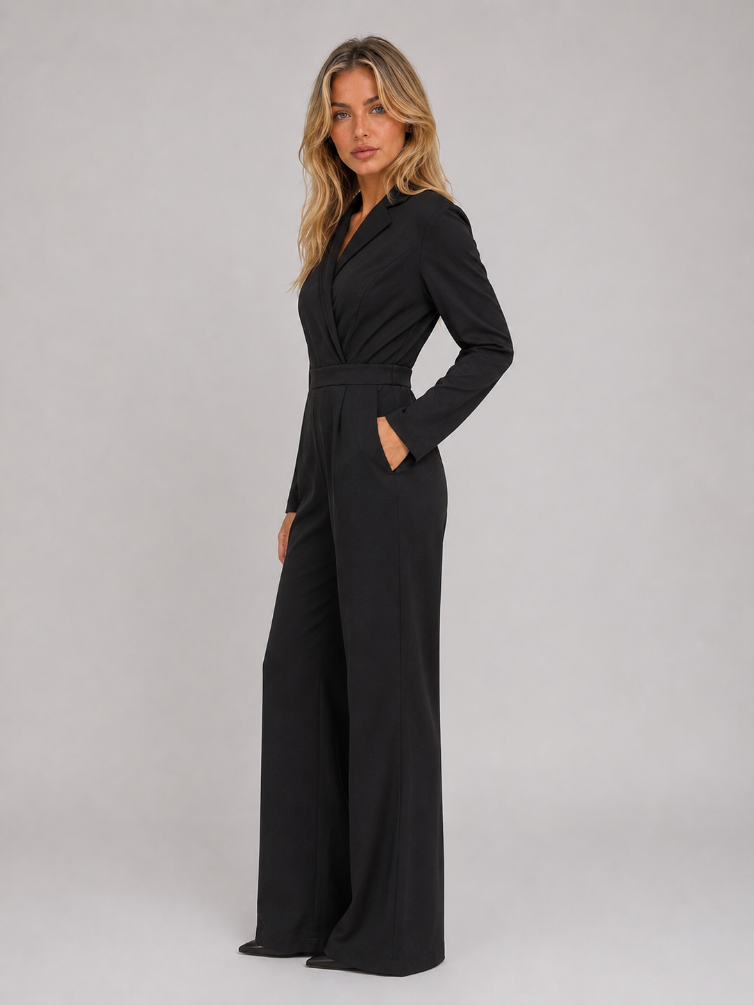 Woman wearing black belted tailored wrap front wide leg jumpsuit with long sleeves and pockets, standing against neutral background