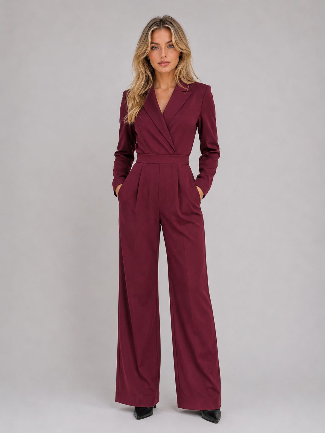 Woman wearing burgundy wrap front belted tailored jumpsuit with long sleeves and wide leg pants