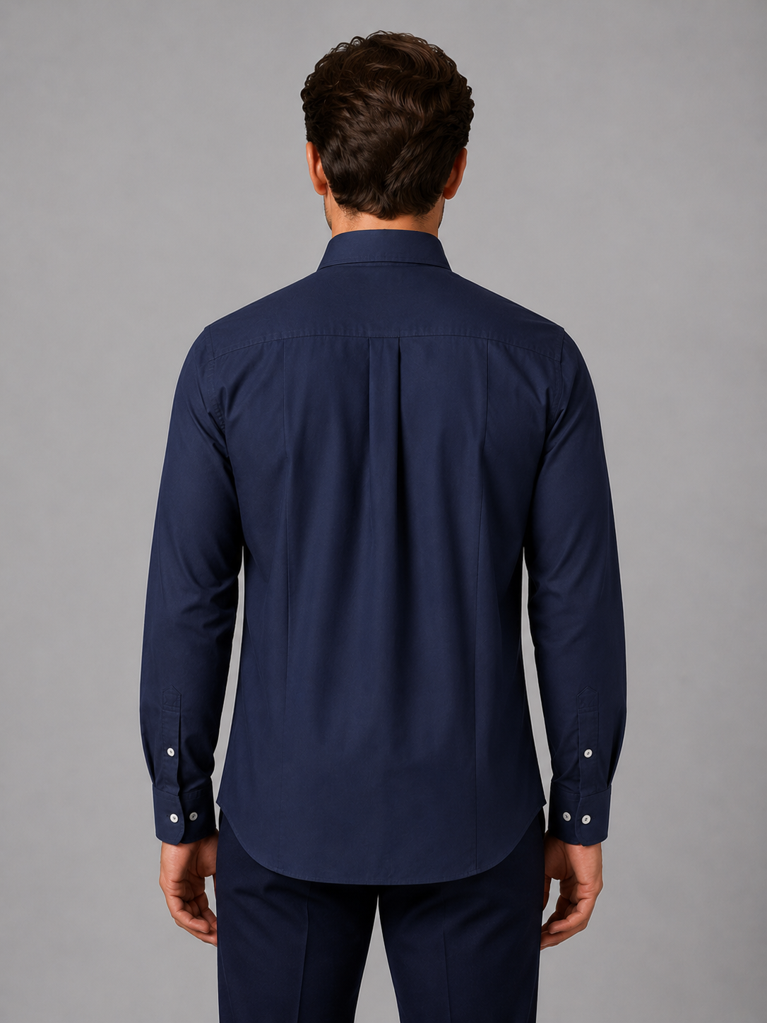 Man wearing navy blue long sleeve button-down collar shirt, rear view, against gray background