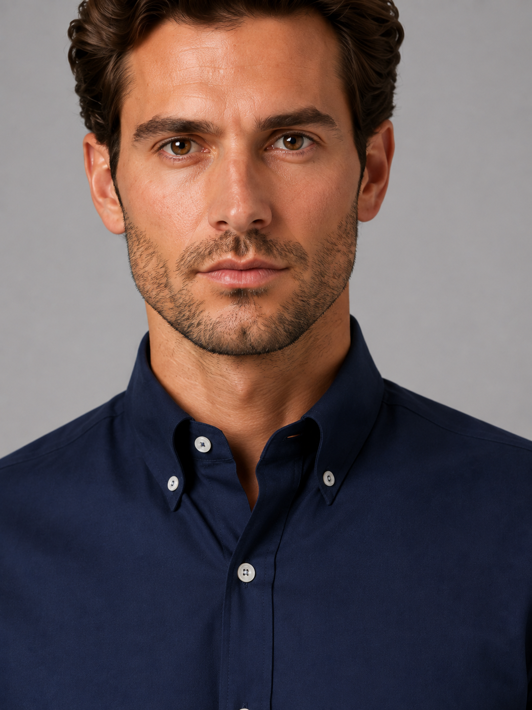 Man wearing dark navy button-down collar long sleeve shirt with white buttons, professional headshot against gray background