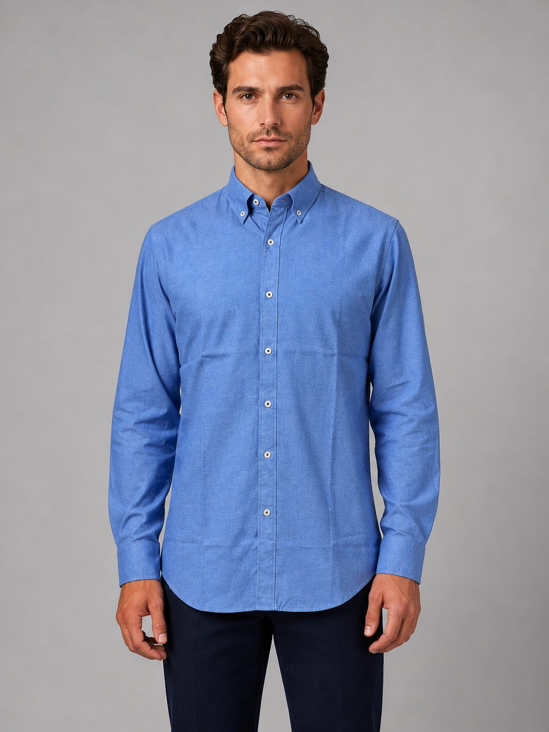 Man wearing blue button-down collar long sleeve shirt with white buttons and dark navy trousers against gray background