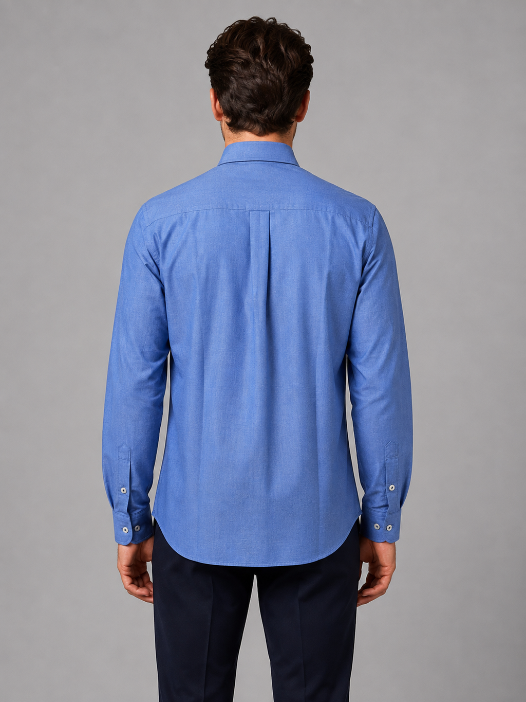 Man wearing blue button-down collar long sleeve shirt with dark pants, shown from back view