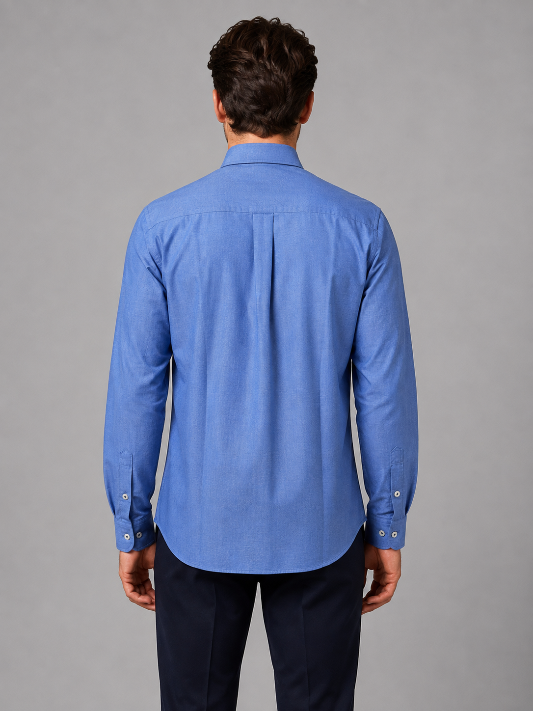 Man wearing blue button-down collar long sleeve shirt with dark pants, shown from back view
