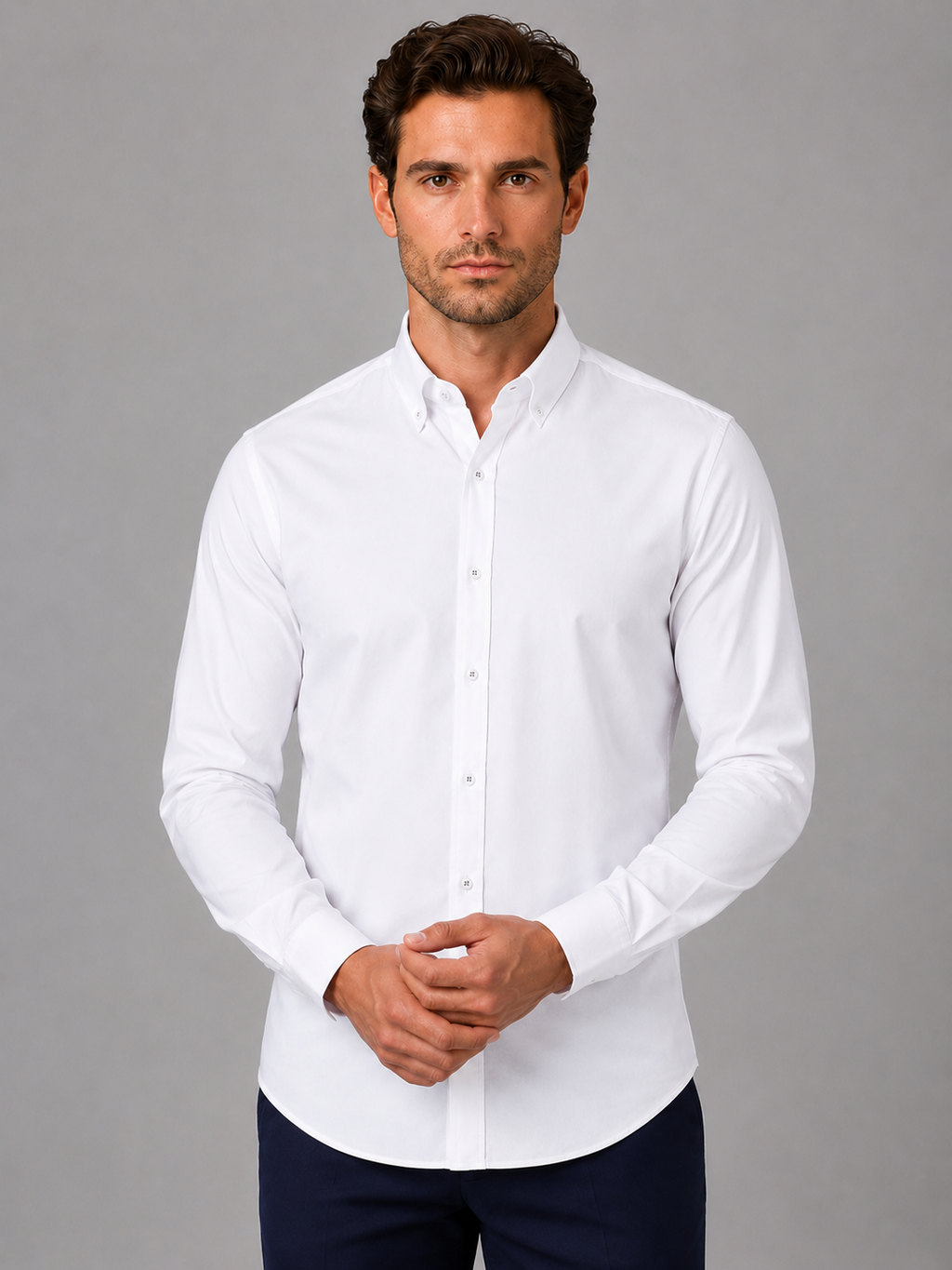 Man wearing white long sleeve button down collar dress shirt with dark navy pants against gray background