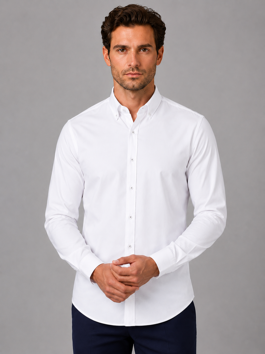 Man wearing white long sleeve button down collar dress shirt with dark navy pants against gray background