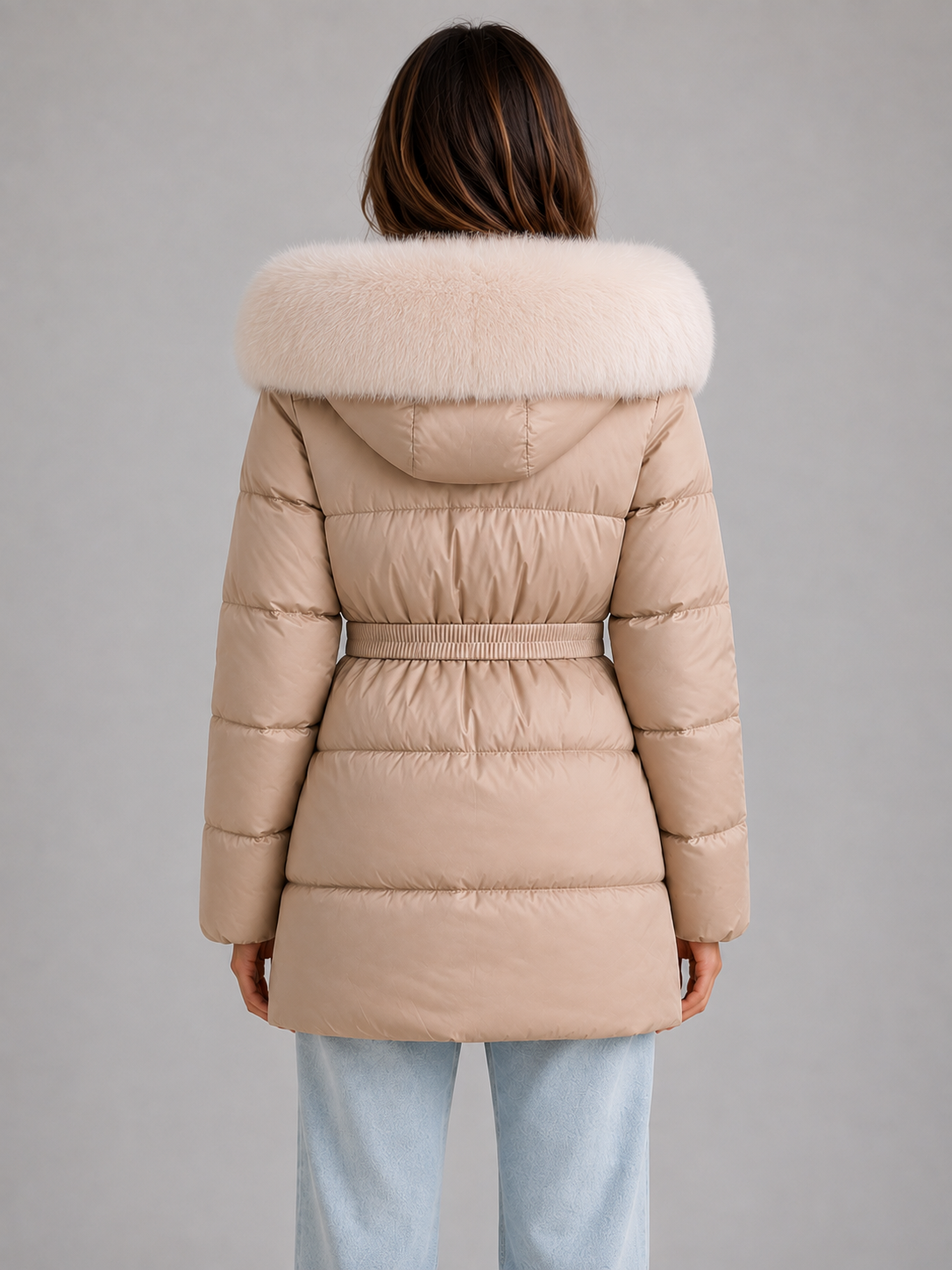 Woman wearing beige belted puffer jacket with white faux fur trim hood and hooded neckline, shown from back view wearing light blue jeans